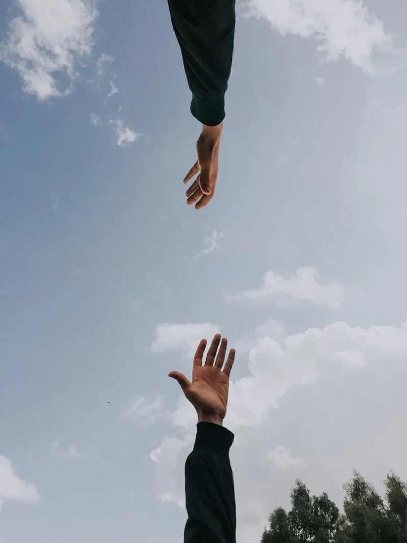Two hands reaching toward each other against the sky