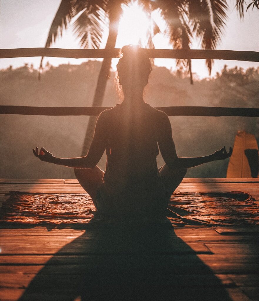 Silhouette of a person meditating on a wooden deck at sunset