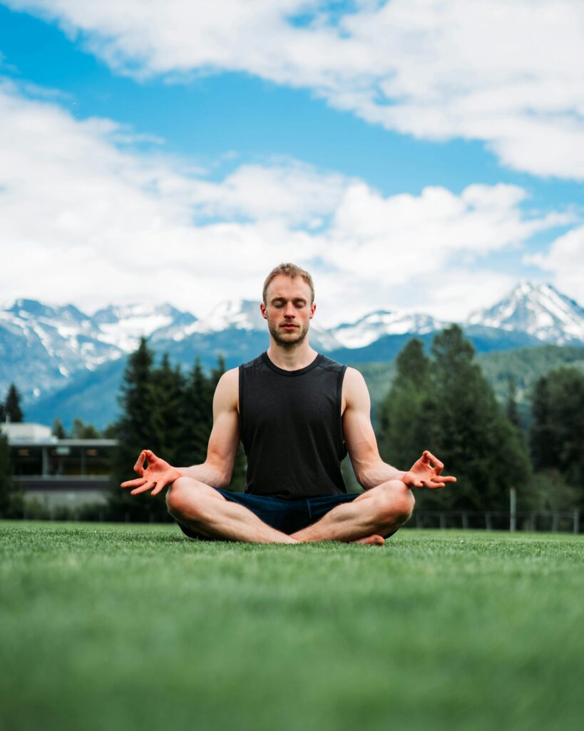 A man meditating on grass in front of snowy mountains